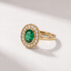 K14 yellow gold ring with an oval-cut emerald and round diamond halo