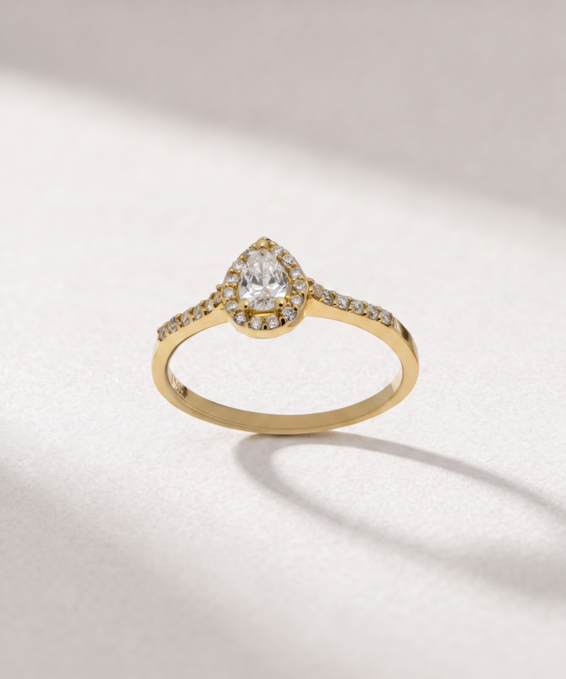 Front view of a K14 yellow gold ring with a pear-cut center diamond and surrounding diamond halo