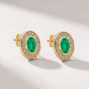 Angled view of oval-cut emerald and diamond halo earrings in K14 yellow gold
